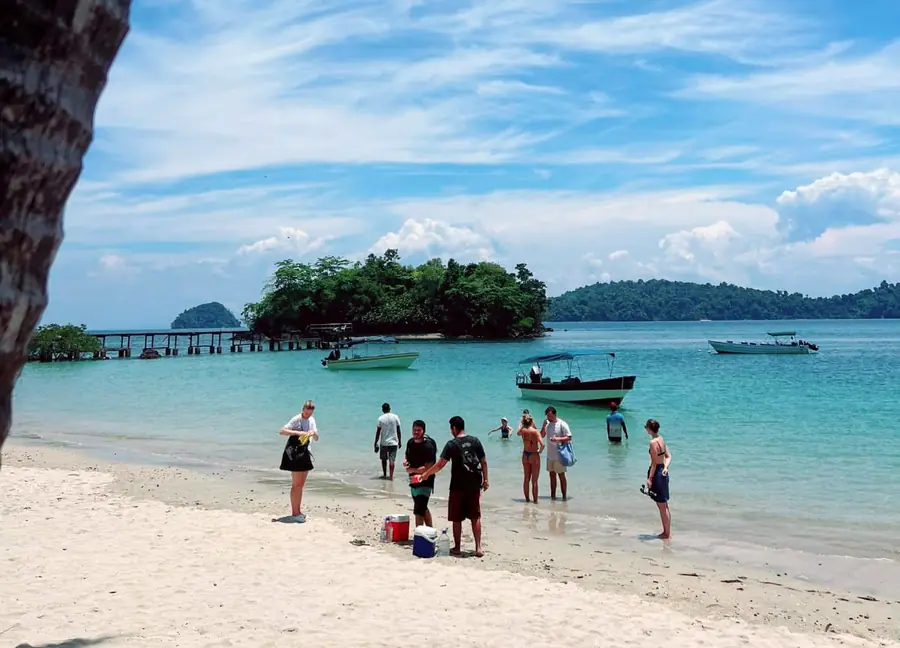 Visitors in the shallow turquoise water of a white-sand beach in Coiba National Park